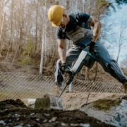 Man using a jackhammer in front of a wire fence