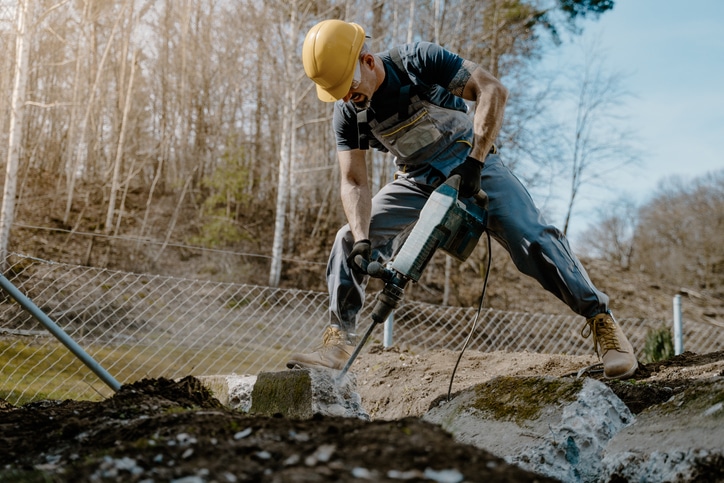 Man using a jackhammer in front of a wire fence